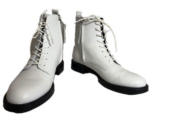 Puede incluir: Un par de botas de cuero blanco con suelas negras. Las botas tienen cordones y cremalleras laterales. Las botas son de un estilo clásico, adecuadas para varios atuendos.