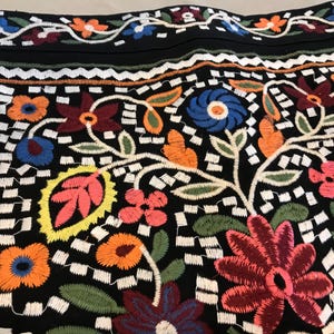 Puede incluir: Tela negra con un patr&oacute;n floral bordado de colores. El dise&ntilde;o presenta una variedad de flores, hojas y enredaderas en tonos de rojo, azul, verde, amarillo y naranja.