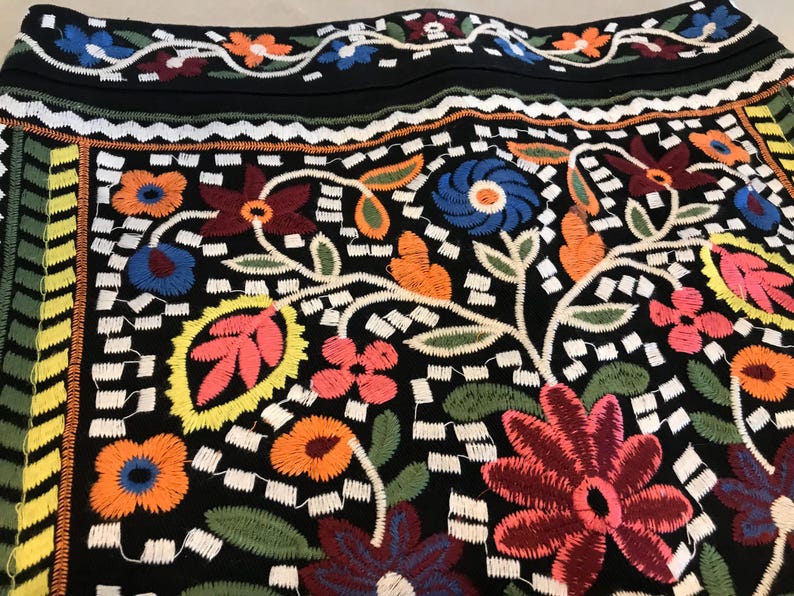 Puede incluir: Tela negra con un patr&oacute;n floral bordado de colores. El dise&ntilde;o presenta una variedad de flores, hojas y enredaderas en tonos de rojo, azul, verde, amarillo y naranja.
