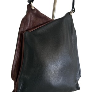 Puede incluir: Un bolso de hombro de cuero negro con interior marr&oacute;n oscuro. El bolso tiene un dise&ntilde;o simple y sin estructura con una correa larga y delgada de color negro. El bolso cuelga de un soporte de metal plateado.