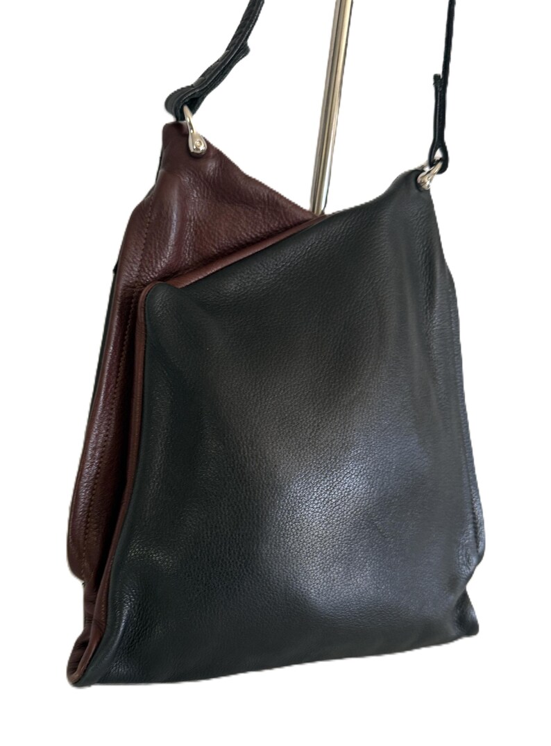 Puede incluir: Un bolso de hombro de cuero negro con interior marr&oacute;n oscuro. El bolso tiene un dise&ntilde;o simple y sin estructura con una correa larga y delgada de color negro. El bolso cuelga de un soporte de metal plateado.