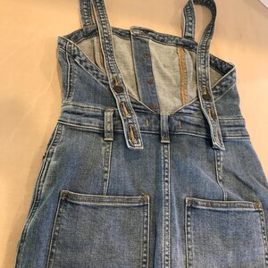 Peut inclure: Une robe en jean bleu avec des bretelles r&eacute;glables et deux grandes poches &agrave; l'arri&egrave;re.