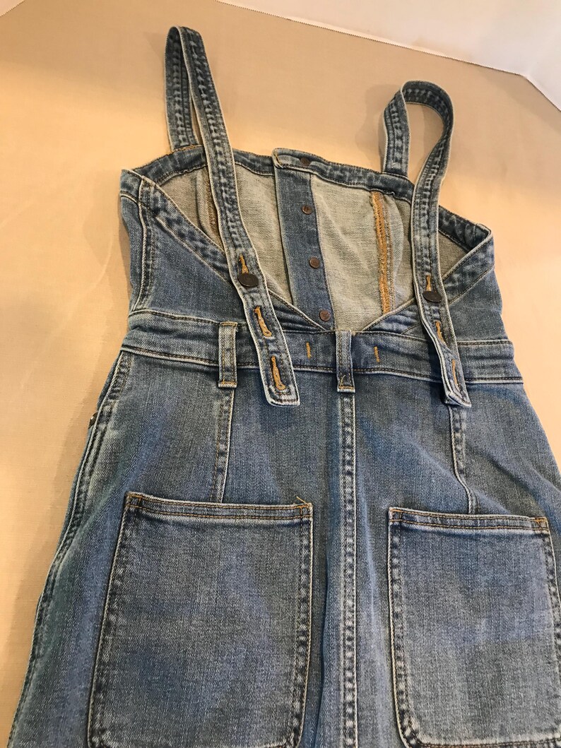 Peut inclure: Une robe en jean bleu avec des bretelles r&eacute;glables et deux grandes poches &agrave; l'arri&egrave;re.