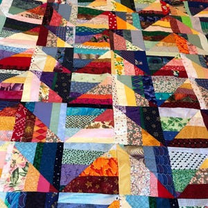 May include: A colorful patchwork quilt with a variety of fabrics and patterns. The quilt is made up of squares and triangles, and the colors include red, blue, green, yellow, orange, and purple.