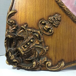 May include: Close-up of a gold-toned ornate frame with intricate carvings and a woodgrain finish.