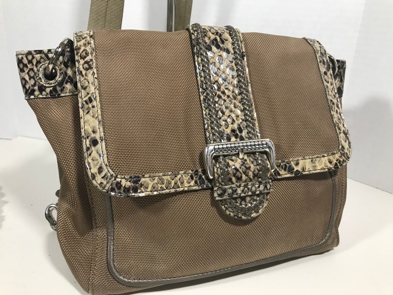 Puede incluir: Un bolso de hombro de lona marr&oacute;n con ribete y hebilla de estampado de piel de serpiente. El bolso tiene cierre de solapa y asa superior.