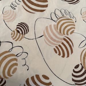 Puede incluir: Tela color crema con un patrón repetido de esferas a rayas marrones y beige conectadas por líneas negras curvas. Las esferas varían en tamaño y tono, creando un diseño dinámico y retro. La tela tiene un aspecto ligeramente texturizado.