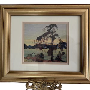 Pode incluir: Impressão de arte emoldurada de uma paisagem com uma árvore silhuetada em frente a um lago e montanhas. A obra de arte está em uma moldura dourada com um passe-partout branco. A impressão tem uma estética vintage.