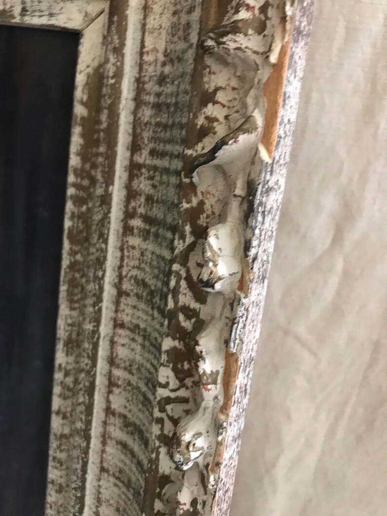 May include: Close-up of a white wooden picture frame with a distressed finish. The frame has a decorative, ornate edge with a raised design.
