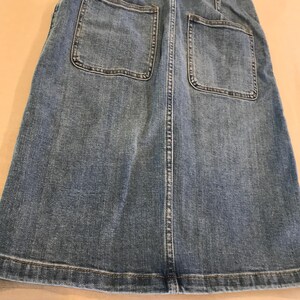Peut inclure: Une jupe en jean bleu avec deux grandes poches plaqu&eacute;es &agrave; l'arri&egrave;re. La jupe a une fermeture boutonn&eacute;e et zipp&eacute;e &agrave; l'avant.