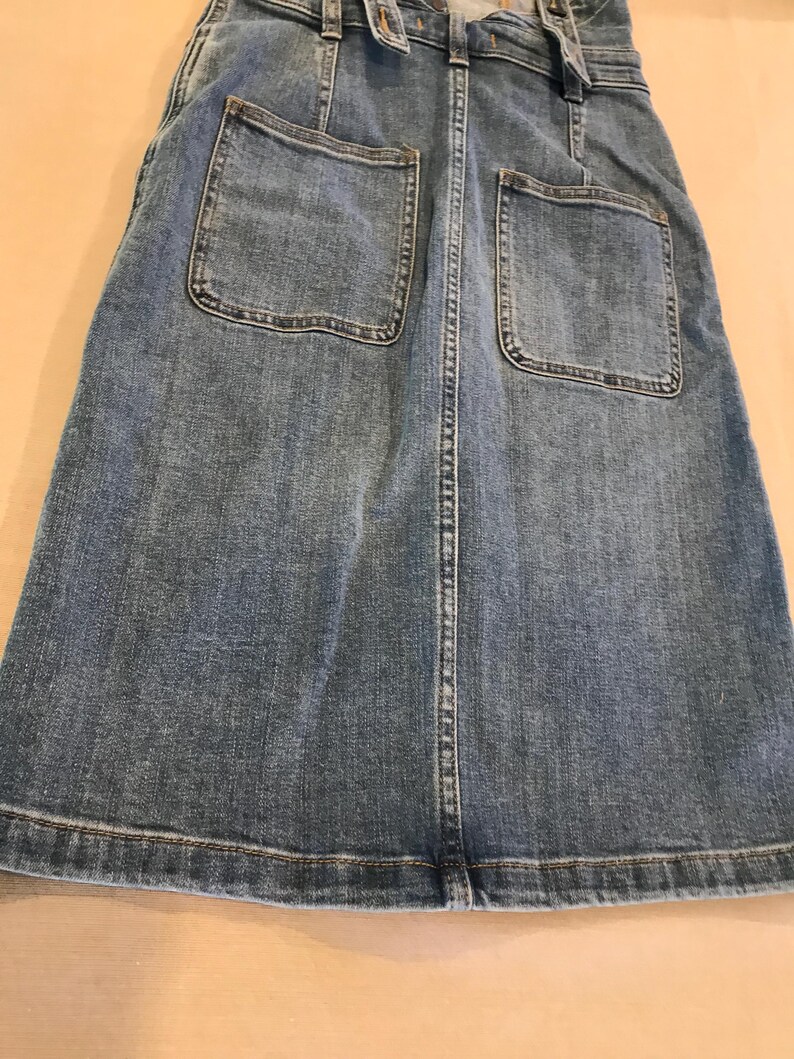 Peut inclure: Une jupe en jean bleu avec deux grandes poches plaqu&eacute;es &agrave; l'arri&egrave;re. La jupe a une fermeture boutonn&eacute;e et zipp&eacute;e &agrave; l'avant.