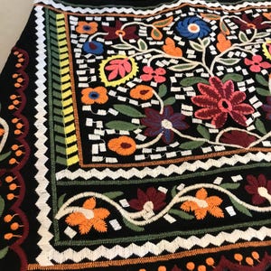Puede incluir: Una falda negra con bordado floral de colores. El bordado presenta una variedad de flores, hojas y patrones geom&eacute;tricos en tonos de rojo, naranja, amarillo, verde, azul y blanco. La falda tiene un dobladillo festoneado.