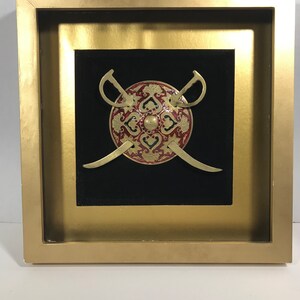 May include: A framed wall art piece featuring a gold shield with red and gold floral designs and two crossed swords.