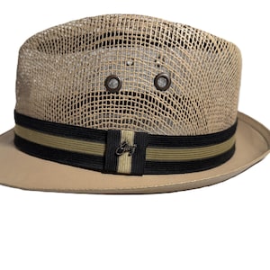 May include: Tan fedora hat with a mesh crown and a solid brim. The hat features a black and olive green striped band with a small metal emblem. Two eyelets are visible on the crown.
