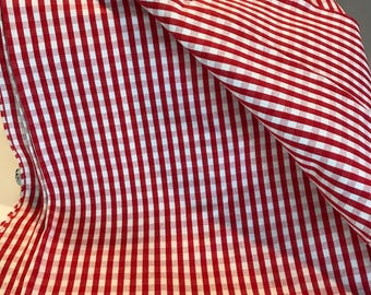 May include: Red and white gingham fabric with a checkered pattern. The fabric is folded in half and the edges are visible.