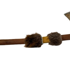 May include: A decorative tomahawk with a wooden handle and a metal head. The head features ornate carvings and a hammer on the opposite side. The handle is adorned with fur and a yellow leather wrap.