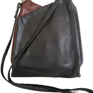 Puede incluir: Bolso de hombro de cuero negro y marr&oacute;n con una correa larga y delgada. El bolso tiene un aspecto texturizado y un interior marr&oacute;n en contraste. La correa tambi&eacute;n es negra y parece ser ajustable.