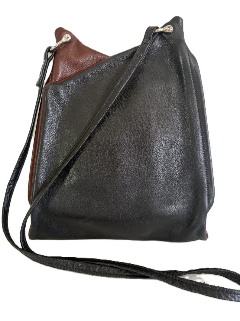 Puede incluir: Bolso de hombro de cuero negro y marr&oacute;n con una correa larga y delgada. El bolso tiene un aspecto texturizado y un interior marr&oacute;n en contraste. La correa tambi&eacute;n es negra y parece ser ajustable.