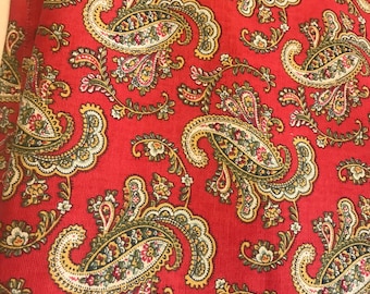 May include: Red fabric with a paisley pattern. The paisley design is in shades of green, yellow, and white.
