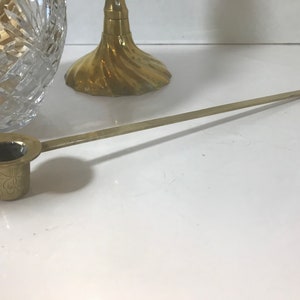 May include: A brass candle snuffer with a long handle and a decorative floral design on the base.