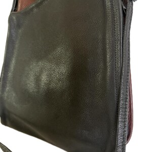 Puede incluir: Un bolso de hombro de cuero negro con una correa larga. El bolso tiene forma redondeada y cierre de cremallera. El interior es de color marr&oacute;n oscuro. El bolso est&aacute; hecho de cuero liso y brillante.