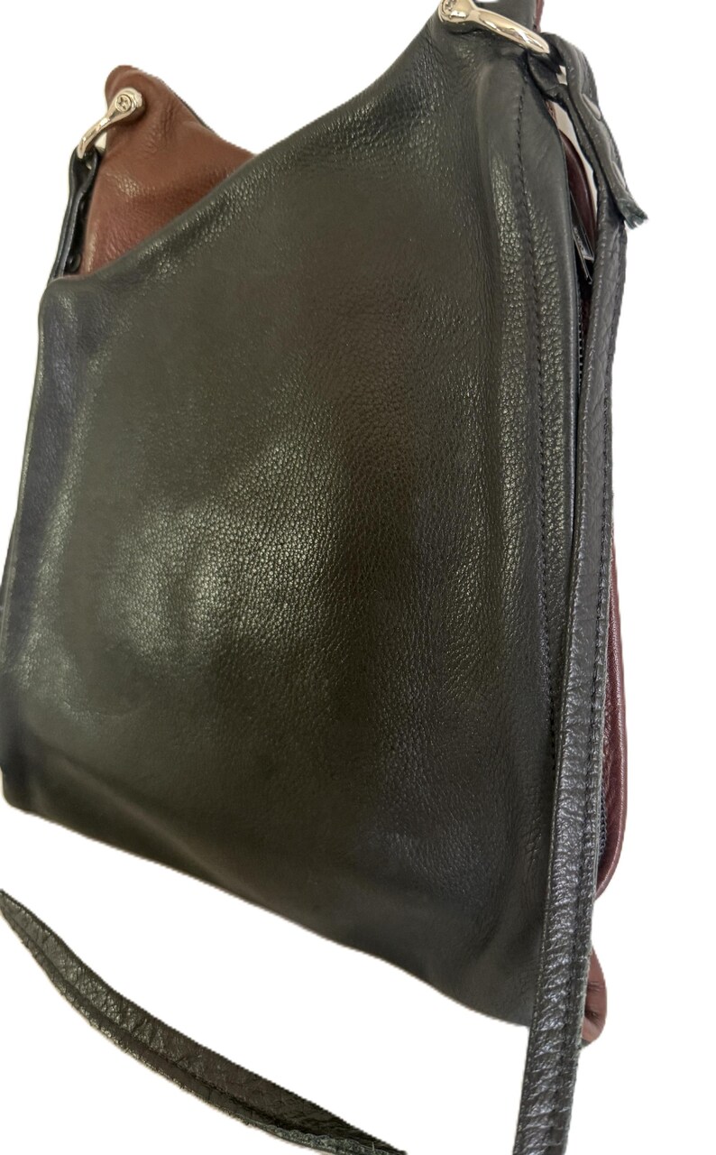 Puede incluir: Un bolso de hombro de cuero negro con una correa larga. El bolso tiene forma redondeada y cierre de cremallera. El interior es de color marr&oacute;n oscuro. El bolso est&aacute; hecho de cuero liso y brillante.
