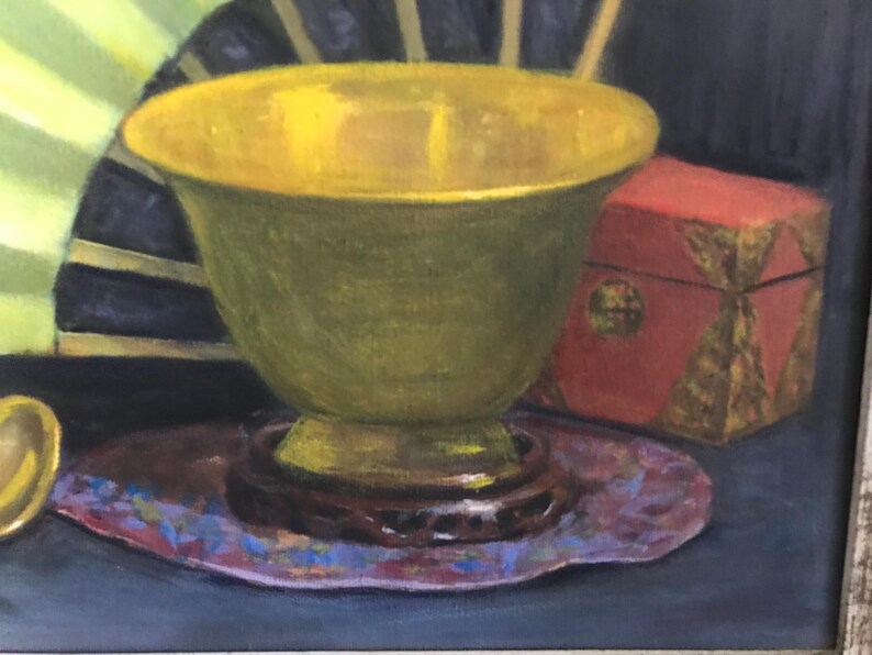 May include: A green ceramic bowl with a gold rim sits on a purple and blue patterned coaster. A red box with gold accents is behind the bowl.