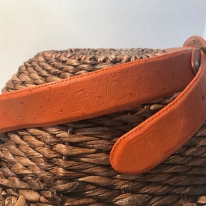 Op de afbeelding: Een bruine leren riem met een gestructureerd oppervlak. De riem is dubbelgevouwen en geplaatst op een geweven oppervlak.