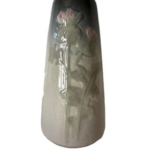 May include: A tall, ceramic vase with a flared shape. The vase features a gradient of colors, transitioning from a dark, glossy black at the top to a light, crackled white at the base. Pink and green floral relief details adorn the vase.