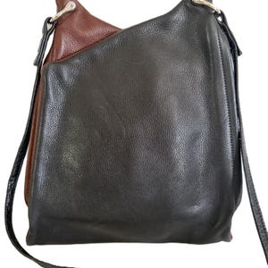Puede incluir: Un bolso de hombro de cuero de dos tonos. El bolso es principalmente negro con un acento marr&oacute;n en la parte superior. Tiene una correa larga y delgada de color negro y herrajes plateados.