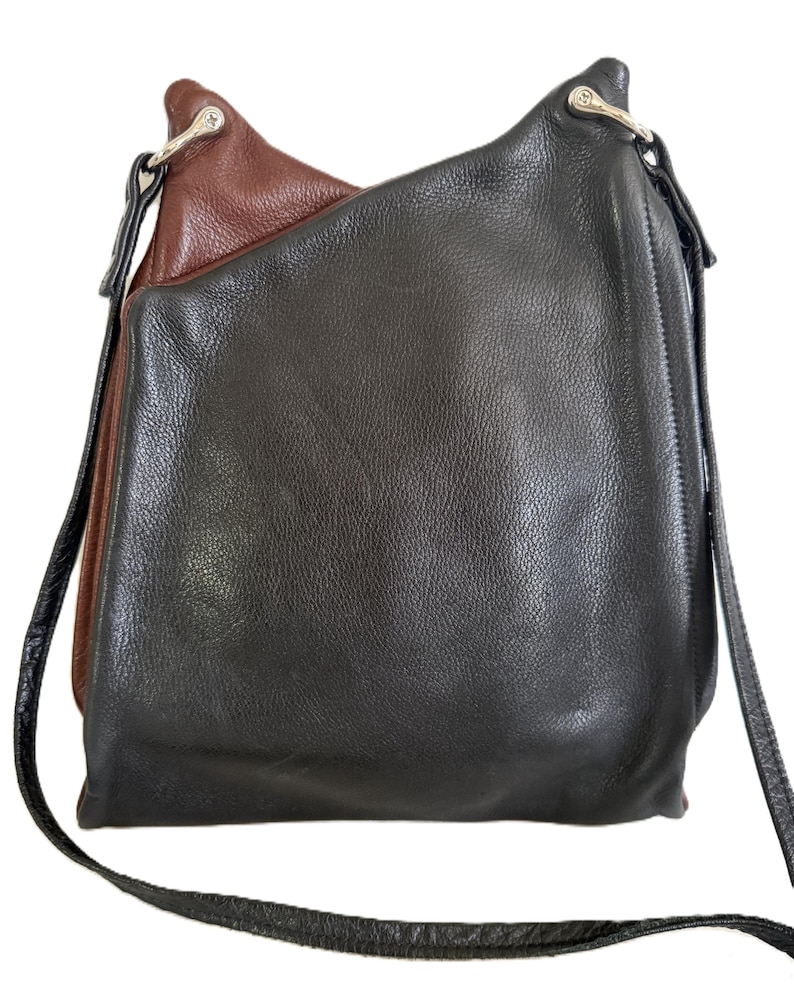 Puede incluir: Un bolso de hombro de cuero de dos tonos. El bolso es principalmente negro con un acento marr&oacute;n en la parte superior. Tiene una correa larga y delgada de color negro y herrajes plateados.
