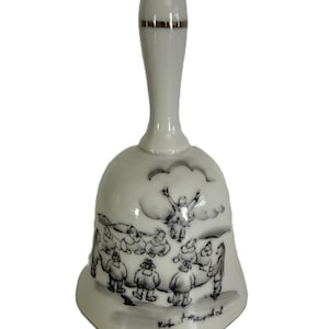 May include: White ceramic bell with a long handle and a flared base. The bell features a black and white illustration of people and clouds. The handle has a gold band near the top. The bell is signed "Robert Maybol".