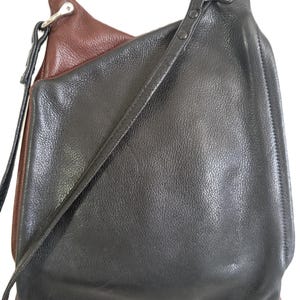 Puede incluir: Bolso de hombro de cuero negro y marr&oacute;n con una correa larga. El bolso tiene una superficie texturizada y un cierre de metal plateado. El interior del bolso es marr&oacute;n y el exterior es negro.