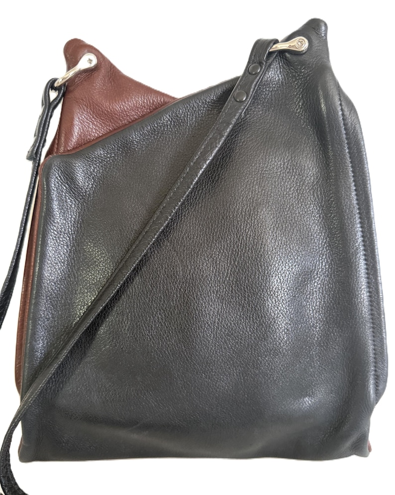 Puede incluir: Bolso de hombro de cuero negro y marr&oacute;n con una correa larga. El bolso tiene una superficie texturizada y un cierre de metal plateado. El interior del bolso es marr&oacute;n y el exterior es negro.