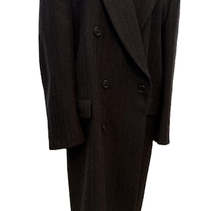 May include: A dark gray double-breasted overcoat. The coat features a notched lapel, two rows of buttons, and a long length. The coat has two front pockets and a tailored fit. The sleeves have buttons at the cuffs. The coat is displayed on a white background.