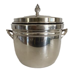 May include: A silver-colored ice bucket with a lid and decorative handles. The bucket has a rounded body and a beaded trim around the middle. The lid is topped with a decorative finial.