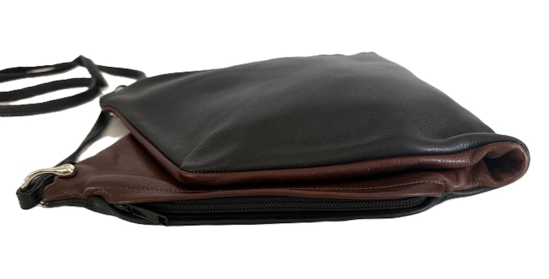 Puede incluir: Bolso bandolera de cuero negro y marr&oacute;n con correa negra. El bolso tiene cierre de cremallera y un dise&ntilde;o en capas, con la capa superior en negro y la capa inferior en marr&oacute;n.