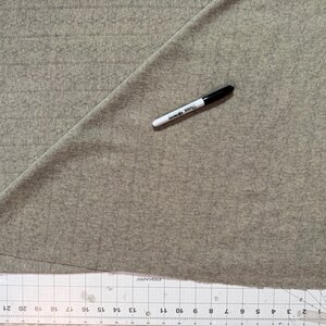 May include: A light beige fabric featuring a subtle vertical cable knit pattern. A black Sharpie marker rests on the fabric surface. A clear plastic ruler is positioned along the bottom edge, showing measurements in inches up to 23 inches.