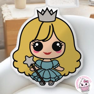 May include: A princess-shaped pillow with a cartoon design. The princess has blonde hair, a silver crown, and a blue dress. She holds a star-shaped wand. The pillow has a white background and a black outline. A cupcake logo is in the bottom right corner.