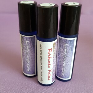 Puede incluir: Tres frascos de vidrio azul con tapas negras y etiquetas blancas. La etiqueta del frasco del centro dice "Varicose Veins" e incluye instrucciones para "Rodar sobre el área afectada dos veces al día". Las etiquetas de los otros dos frascos dicen "Live Love Oils".