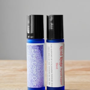 May include: Two blue glass roller bottles with black caps. The bottle on the left has a label that says "Live.Love.Oils". The bottle on the right has a label that says "Roid Rage Thyroid Support Blend" and "For support of a sluggish thyroid roll onto area of the thyroid in the am. Contains peppermint, clove, lemongrass."