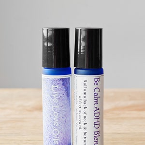 May include: Two blue glass roller bottles with black lids. The bottles are labeled "Be Calm ADHD Blend" and "Live Love Oils".
