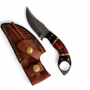 May include: A Damascus steel knife with a curved blade and a handle featuring black, red, and gold accents. The knife is accompanied by a brown leather sheath with brass button closures.