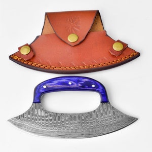 Op de afbeelding: Een blauwe en zilveren Damascus-cleaver met een paarse handgreep en een bruine leren schede.