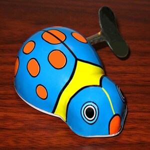May include: A wind-up toy shaped like a ladybug. The toy is painted blue with orange spots and yellow accents. It has a wind-up key on the side and is set against a wooden surface.