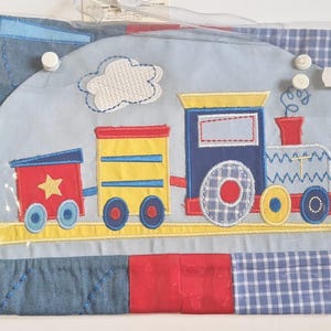 Puede incluir: Un diseño de tren colorido sobre un fondo azul claro. El tren tiene una cabina roja con una estrella amarilla, vagones amarillos y azules y una locomotora azul. El fondo es de mezclilla y cuadros vichy.