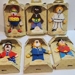 Puede incluir: Conjunto de seis marionetas de madera con ropa colorida y detalles pintados. Cada marioneta tiene una cuerda atada a su mano y una pequeña base de madera. Las marionetas están empaquetadas en cajas individuales con el nombre de la marca "Hampelhans" y el texto "Let's have a sticky day!"