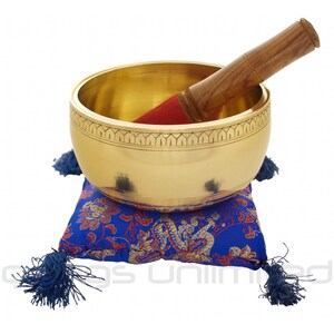 May include: A gold singing bowl with a wooden striker and a blue and red patterned cushion. The bowl has an intricate design around the rim.