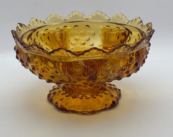 May include: Amber glass candle holder with three candle cups and a scalloped rim. The holder has a textured, bubbled surface and a pedestal base.
