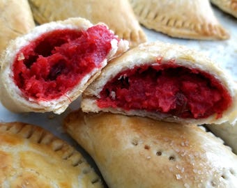 May include: Close-up of several golden brown pastries filled with a bright red sweet filling. The pastries are arranged on a white surface.